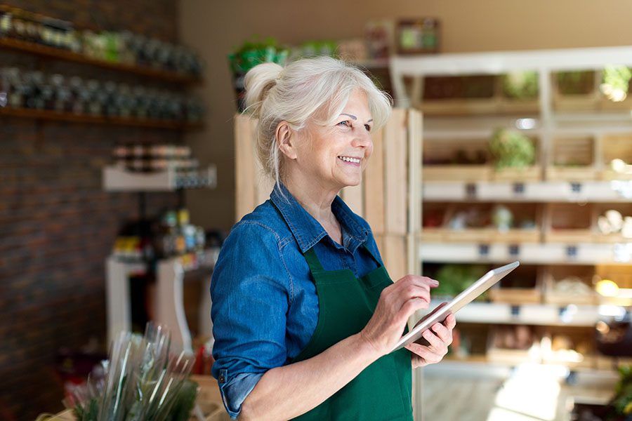 Business Insurance - Smiling Mature Business Owner Standing in Her Shop Using a Tablet