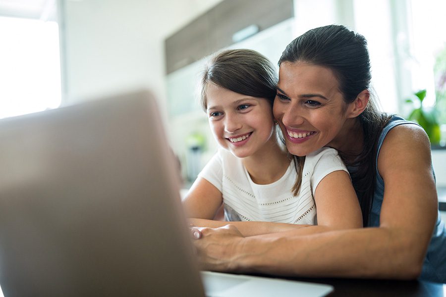 Client Center - Smiling Mother and Daughter Using a Laptop at Home