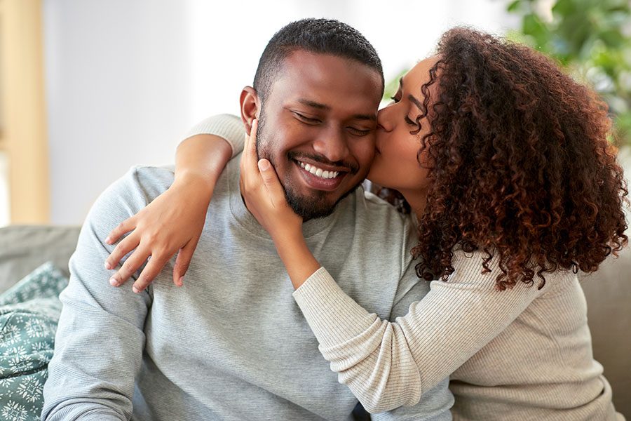 Personal Insurance - Wife Kissing Her Husband While Sitting on the Sofa at Home